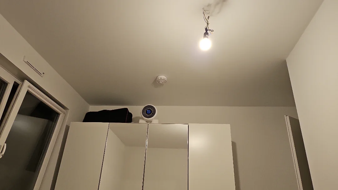 A white wardrobe is against the wall, with an air purifier and a black bag placed on top.
